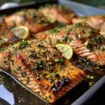 Side view of grilled salmon fillet with a golden crust, adorned with lemon wedges.
