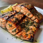 A side view of grilled salmon topped with lemon zest and fresh dill.