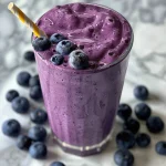 Freshly made blueberry smoothie in a clear glass, garnished with blueberries and yogurt.