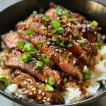 Detailed shot of a delicious crispy beef rice bowl featuring minced garlic and sliced green onions.