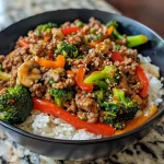 A side view of a savory stir-fried beef bowl, showcasing broccoli, bell peppers, and zucchini.