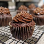 A close-up side view of moist mini chocolate cupcakes topped with smooth chocolate cream cheese frosting.