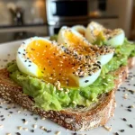Delicious avocado toast featuring a creamy green spread and a halved hard-boiled egg on top.