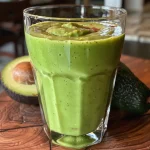 Side view of a creamy avocado smoothie in a glass, garnished with a slice of avocado.