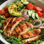 Vibrant chicken salad bowl featuring diced cucumbers, cherry tomatoes, and sunflower seeds on top.