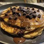 Close-up view of fluffy chocolate chip pancakes, stacked and topped with melted chocolate chips.