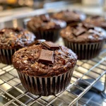 Close-up view of a chocolate muffin with a glossy top and chocolate chunks.