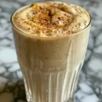 Close-up side view of a creamy apple banana smoothie in a clear glass with fruit pieces visible.