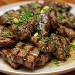 A close-up side view of juicy garlic butter steak bites, glistening with melted butter and herbs.
