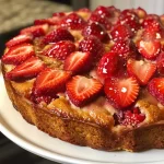 Delicious strawberry yogurt cake slice with vibrant red strawberries on a white plate.