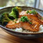 A close-up view of a Teriyaki Salmon Bowl featuring salmon, broccoli, and rice.