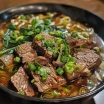 Close-up view of a bowl of Chili Oil Garlic Noodles with garnishes.