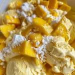 Close-up of vibrant yellow mango ice cream in a bowl, with a spoon resting beside it.