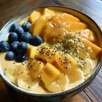 A side view of a vibrant Mango Banana Smoothie Bowl topped with fresh fruit and granola.