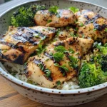 Juicy grilled chicken slices on a bed of broccoli and rice in a bowl.