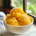 A close-up view of a vibrant yellow No-Churn Mango Sorbet served in a bowl.