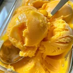 Close-up of creamy yellow mango ice cream in a bowl with diced mango pieces.