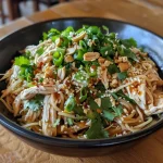 Close-up of cold noodles topped with shredded chicken, cucumber, and peanuts.