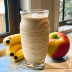 A close-up view of a creamy Apple Banana Oat Smoothie in a glass, with visible oats and ice cubes.