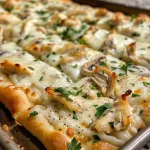 Close-up view of a Chicken Alfredo flatbread topped with melted cheese and fresh ingredients.