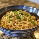 Close-up view of creamy cold sesame noodles topped with green onions and sesame seeds.