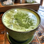 A side view of a frothy matcha latte in a clear glass, with a smooth, creamy texture.