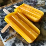 Close-up of vibrant frozen mango popsicles on a wooden surface.