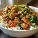 Close-up view of a Honey Garlic Chicken Rice Bowl topped with colorful vegetables.