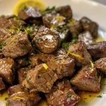 Close-up view of tender beef cubes glistening with lemon butter sauce.