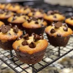 A close-up side view of golden-brown mini banana chocolate chip muffins, garnished with chocolate chips.