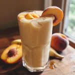 Close-up view of a peach honey yogurt smoothie with ice cubes, peach slices, and a banana slice.