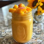 Close-up of a peach mango smoothie in a glass with a straw.