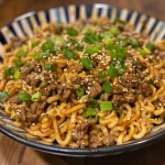 Close-up view of savory Asian ground beef noodles topped with green onions.