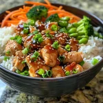 Close-up view of a juicy teriyaki chicken rice bowl with colorful vegetables.