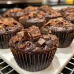 A close-up side view of a moist Ultimate Brownie Muffin with a glossy chocolate topping.