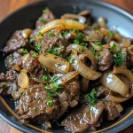 ['Close-up view of juicy beef liver slices sautéed with onions.', 'Side view of a plate featuring cooked beef liver and caramelized onions.', 'Juicy beef liver pieces served with golden-brown sautéed onions.', 'Detailed look at beef liver and onions on a rustic plate.']