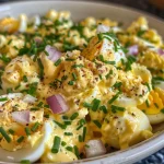 ['Close-up view of a creamy egg salad with herbs and onions.', 'Side photo of vibrant egg salad in a bowl with a sprinkle of herbs.', 'Delicious egg salad displayed with diced red onions and greens.', 'Juicy egg salad with a rich texture, garnished with parsley and chives.']