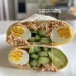 ['Close-up view of cold tuna wraps with visible chunks of tuna and vegetables.', 'Side perspective of two tortilla wraps filled with tuna, cucumber, and hard-boiled eggs.', 'Juicy cold tuna wraps showcasing their colorful ingredients and creamy texture.', 'Deliciously arranged cold tuna wraps with a focus on the ingredients inside.']