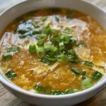 ['Close-up of a bowl of Easy Egg Drop Soup, showcasing golden egg ribbons and green onions.', 'Side view of a steaming bowl of Easy Egg Drop Soup with visible broth and floating egg strands.', 'Detailed view of a homemade Easy Egg Drop Soup with green onion garnish and rich chicken broth.', 'Inviting image of Easy Egg Drop Soup, highlighting texture and vibrant colors of ingredients.']