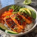['Close-up view of a Healthy Sweet Chili Salmon Bowl topped with fresh vegetables.', 'Side view of a vibrant bowl filled with salmon, rice, and colorful vegetables.', 'Juicy salmon fillet resting on jasmine rice, garnished with sliced cucumber and avocado.', 'A healthy meal featuring salmon and an assortment of vegetables in a bowl.']