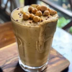 ['Close-up of a creamy chickpea smoothie in a glass with a banana and cinnamon garnish.', 'Side view of a high-protein smoothie made with chickpeas, banana, and peanut butter powder.', 'A delicious chickpea smoothie in a clear glass, displaying a smooth, thick texture.', 'Frosted glass filled with a nutrient-rich chickpea smoothie, featuring a rich golden-brown color.']