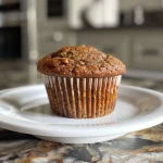 ['Close-up view of a moist high protein muffin with shredded carrots and coconut.', 'Side angle of a delicious, freshly baked muffin highlighting its fluffy texture.', 'Juicy high protein muffin with visible carrot shreds and coconut flakes, set against a neutral background.', 'Detailed close-up of a healthy muffin showcasing its gooey interior and topping.']
