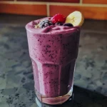 ['Close-up view of a vibrant quinoa smoothie in a glass with bananas and spices.', 'Side view of a creamy quinoa smoothie with ingredients arranged around it.', 'Thick quinoa smoothie in a transparent cup, featuring banana slices on top.', 'Rich and colorful quinoa smoothie with ice cubes and garnished with cinnamon.']