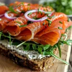 ['Close-up view of a smoked salmon sandwich on rye bread with fresh herbs.', 'Delicious smoked salmon sandwich featuring cream cheese and arugula, side view.', 'Juicy smoked salmon sandwich with red onion and herbs, captured with an iPhone.', 'Tasty smoked salmon sandwich showcasing layers of smoked fish and cream cheese.']