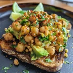 ['Close-up of a vibrant Spicy Chickpea Avocado Toast topped with chili flakes on sourdough bread.', 'A side view of a juicy Spicy Chickpea Avocado Toast showcasing chickpeas and avocado on toasted bread.', 'Detailed shot of a Spicy Chickpea Avocado Toast garnished with fresh herbs and chili flakes, highlighting textures.', 'Delicious Spicy Chickpea Avocado Toast piled high with chickpeas, creamy avocado, and spices on crispy bread.']