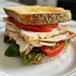 ['A close-up side view of a juicy Turkey Pesto Sandwich on crusty sourdough bread.', 'A succulent Turkey Pesto Sandwich showcasing layers of turkey, provolone, and fresh vegetables.', 'A detailed shot of a Turkey Pesto Sandwich with vibrant ingredients on a rustic table.', 'A side view of a delicious Turkey Pesto Sandwich featuring pesto, turkey, and fresh greens.']