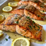 ['A close-up side view of juicy baked salmon fillet drizzled with lemon butter cream sauce.', 'Succulent baked salmon topped with a creamy lemon butter sauce on a white plate.', 'Side angle shot of baked salmon garnished with chopped parsley and lemon slices.', 'Detailed view of a flaky salmon fillet coated in rich lemon butter cream sauce.']