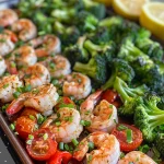['Close-up of vibrant sheet pan spicy garlic shrimp with broccoli and tomatoes.', 'Juicy shrimp with garlic and veggies arranged on a baking sheet.', 'Colorful shrimp and vegetable medley on a pan, garnished with lemon wedges.', 'Mouthwatering shrimp dish featuring broccoli, tomatoes, and green onions.']