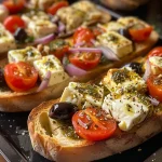 ['A close-up view of Mediterranean Baked Feta Bruschetta topped with shrimp and vegetables.', 'Juicy Mediterranean Baked Feta Bruschetta with vibrant cherry tomatoes and olives on toasted bread.', 'Side view of a delicious bruschetta featuring baked feta, garlic, and shrimp with a pesto drizzle.', 'A plate of Mediterranean Baked Feta Bruschetta garnished with herbs and shrimp, showcasing its vibrant colors.']