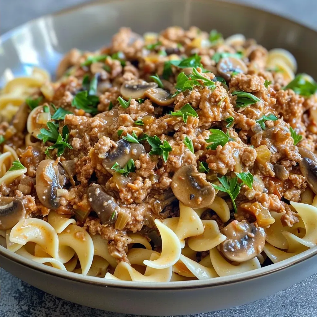 ['Close-up of a delicious ground turkey dinner, featuring ground turkey, diced onions, and mushrooms on a plate.', 'Side view of a hearty ground turkey dish with creamy sauce and parsley garnish.', 'Detailed view of a ground turkey meal with egg noodles, garnished with fresh parsley.', 'Juicy ground turkey mixture with onions and garlic, presented in a bowl.']